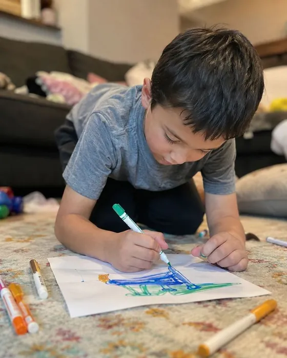 Menino desenhando e colorindo no chão de casa
